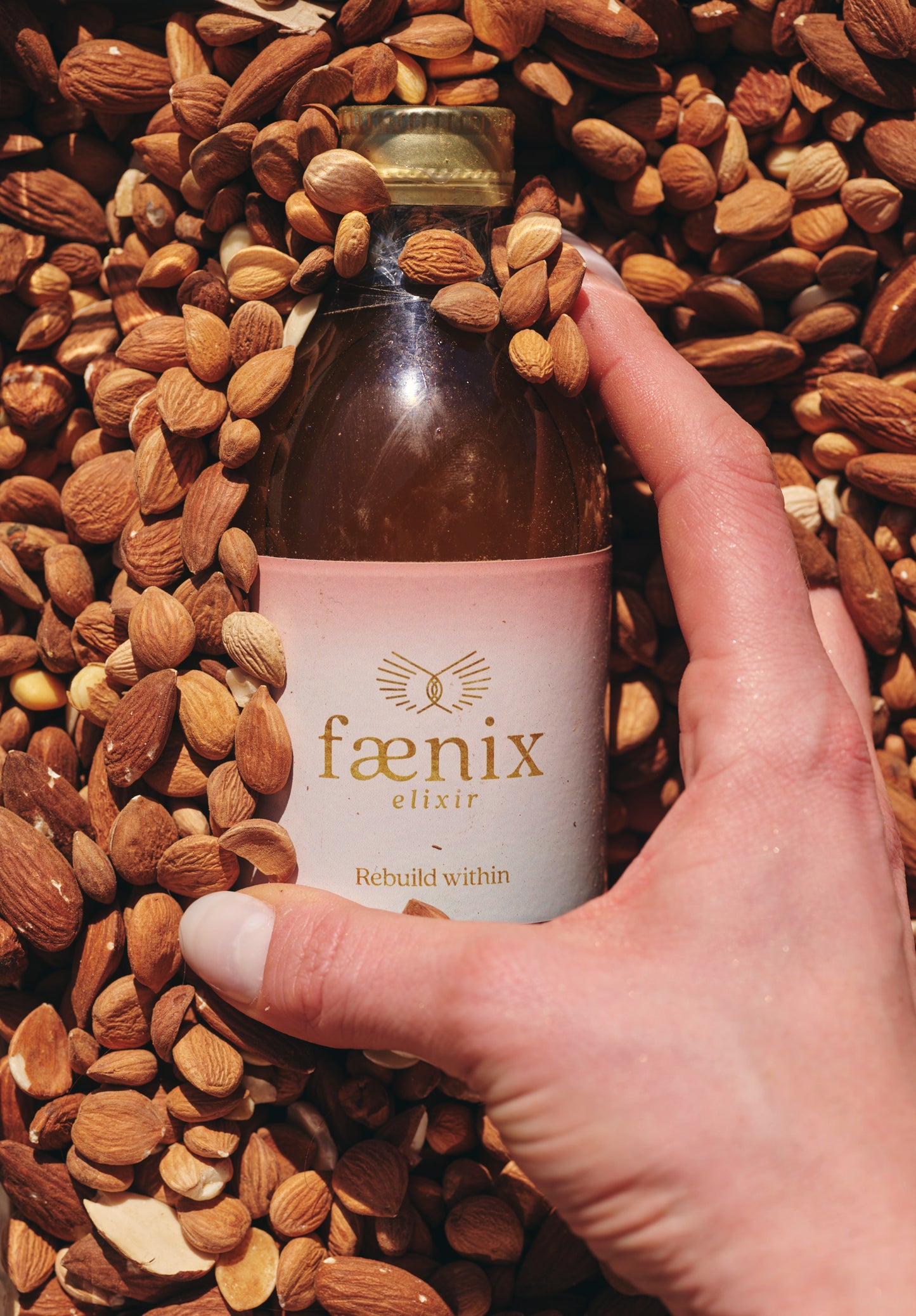 Hand holding a bottle labeled 'faenix elixir' surrounded by almonds
