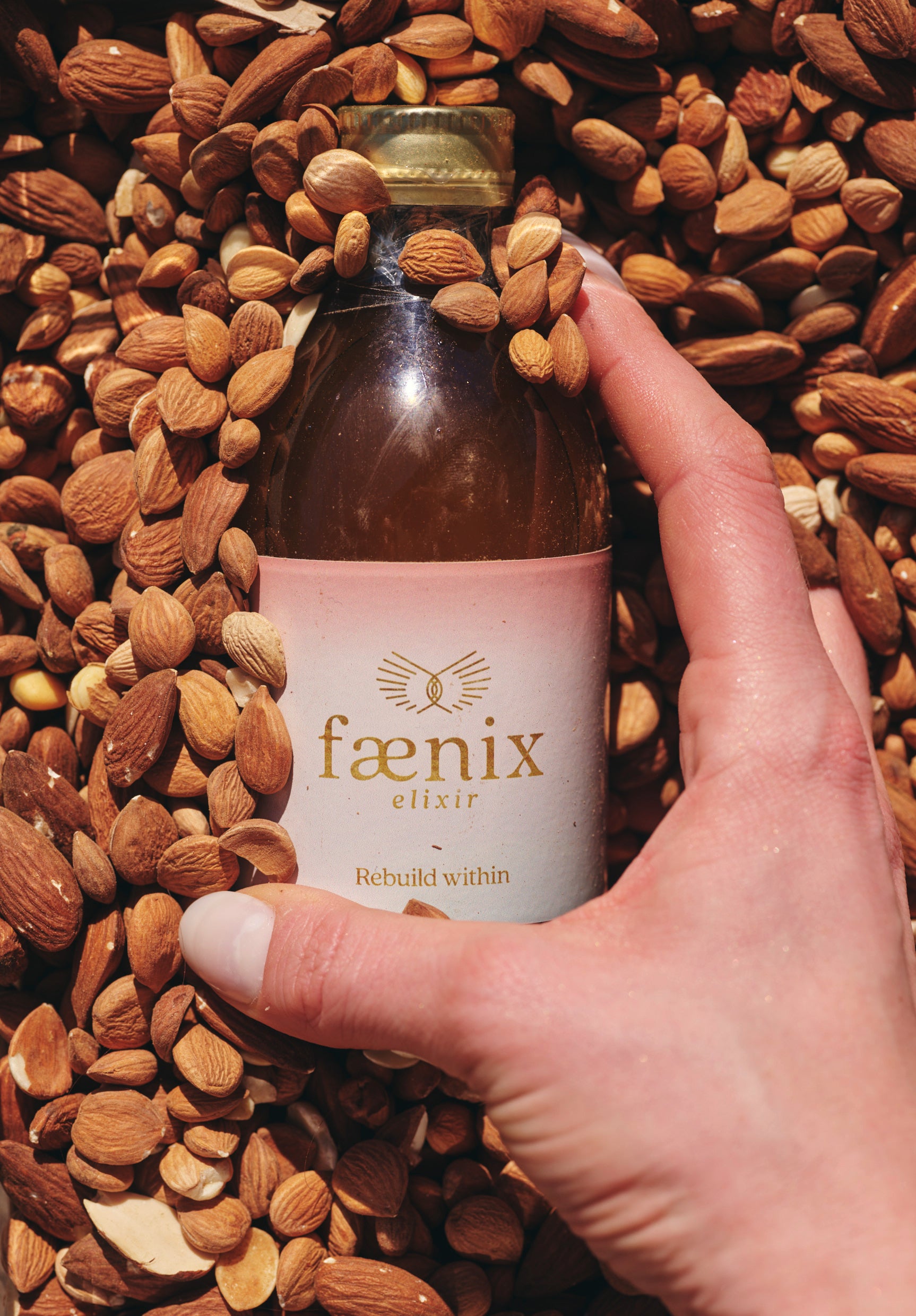 Hand holding a bottle labeled 'faenix elixir' surrounded by almonds