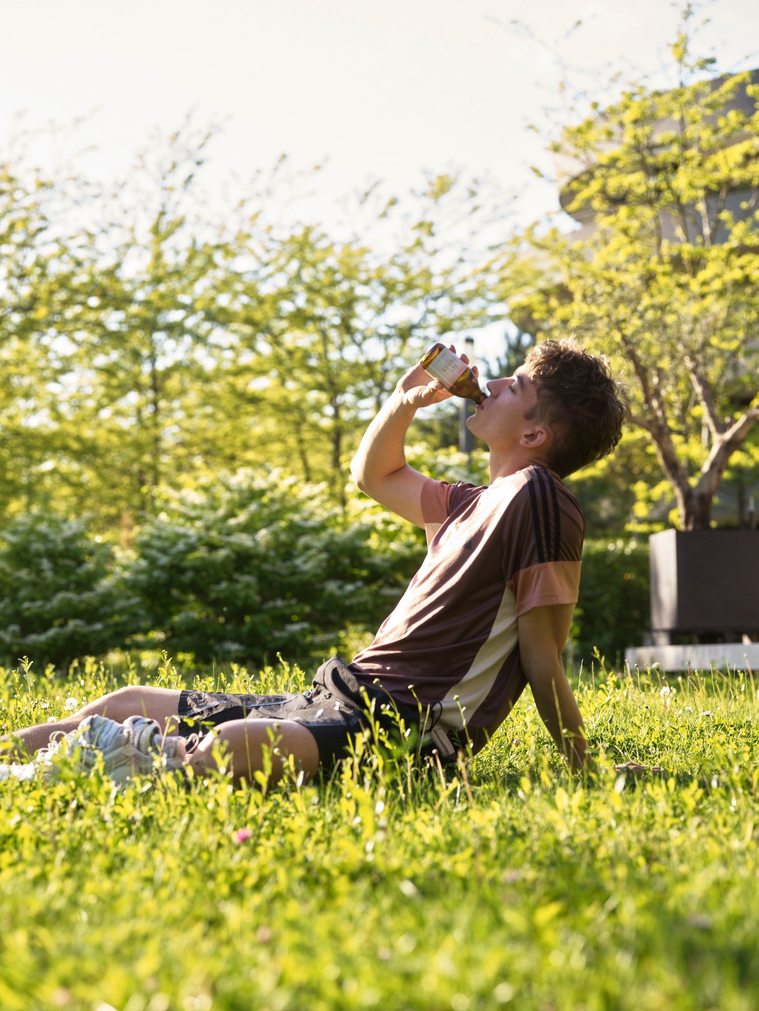 Person sitting on grass in a park, drinking from a bottle