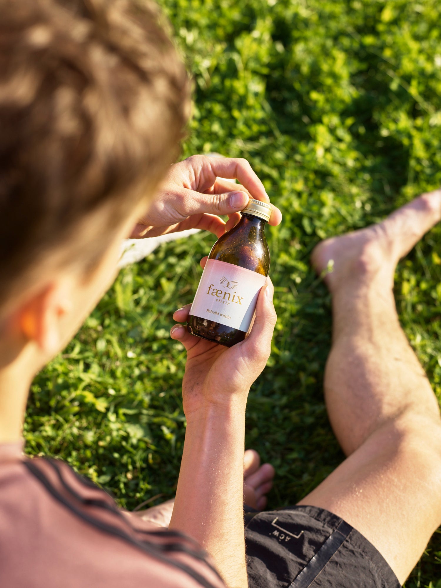 Person sitting on grass holding a small bottle labeled 'Ferrin'.
